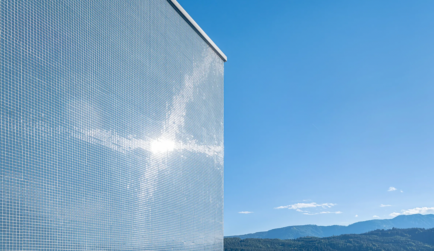 StoVentec glass mosaic façade on a modern house exterior, shining in the sun with a scenic mountain backdrop—showcasing high-performance, design-forward rainscreen cladding.