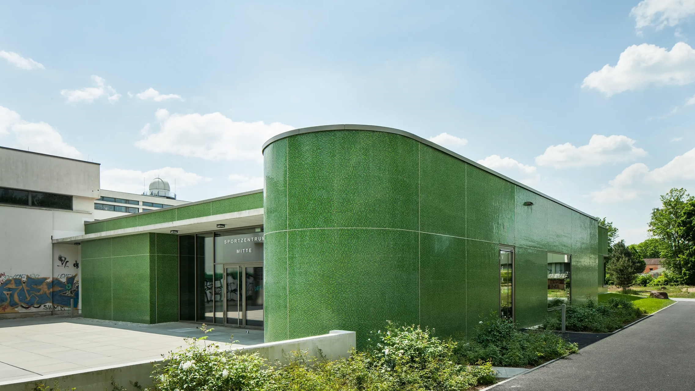 StoVentec green glass mosaic rainscreen system curving along exterior wall of modern sports complex building for durable, vibrant façade design