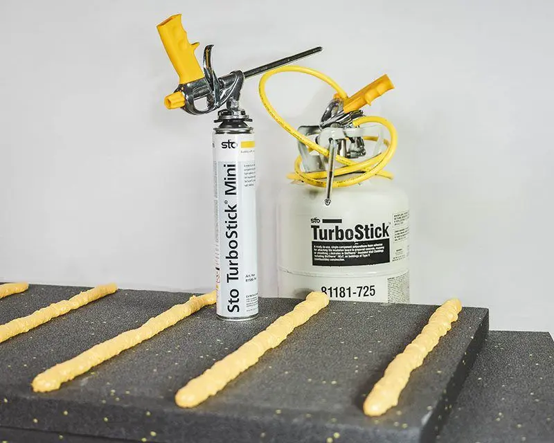Sto TurboStick adhesive shown during application with visible beads of foam, canister mounted on applicator pistol for precise EIFS insulation board installation